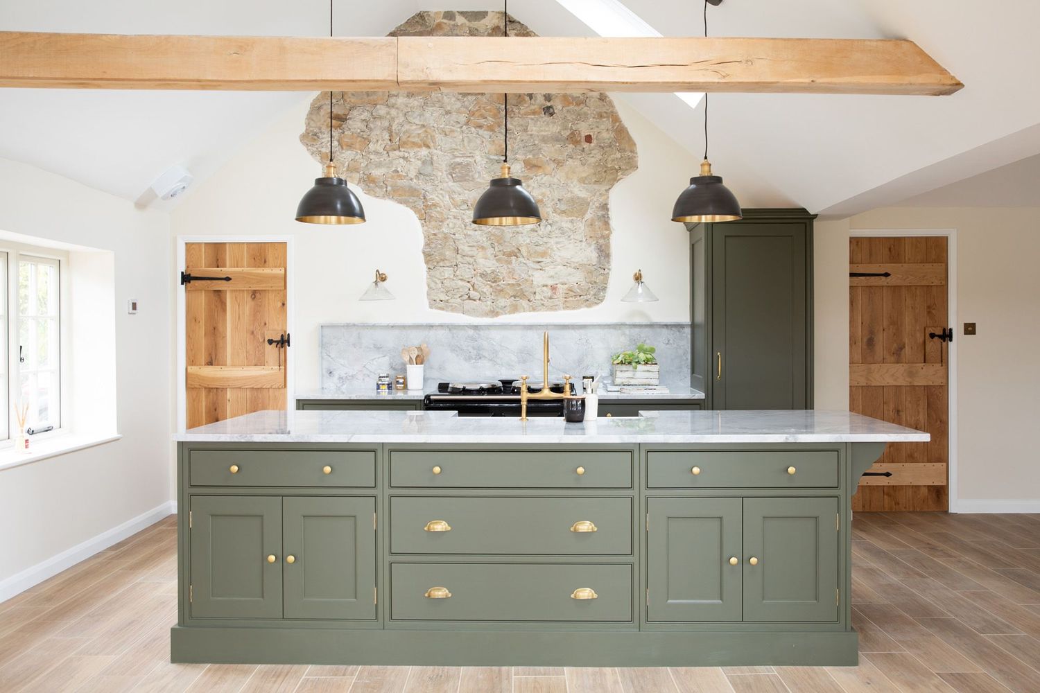 Rustic kitchen with sage green island, exposed stone wall, and wooden beam ceiling detail.