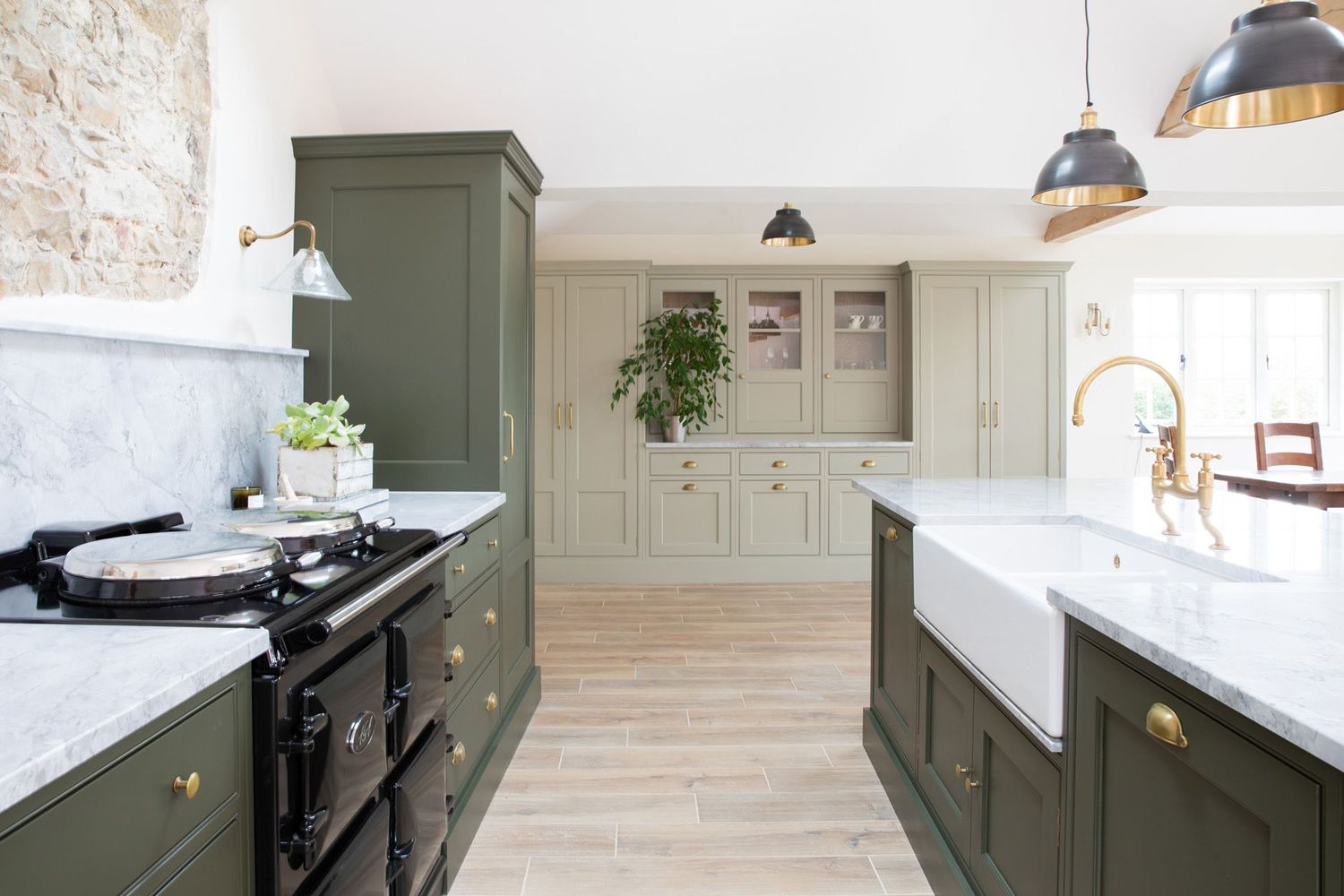 Farmhouse kitchen featuring green cabinetry, white farmhouse sink, and brass fixtures with stone wall accent.