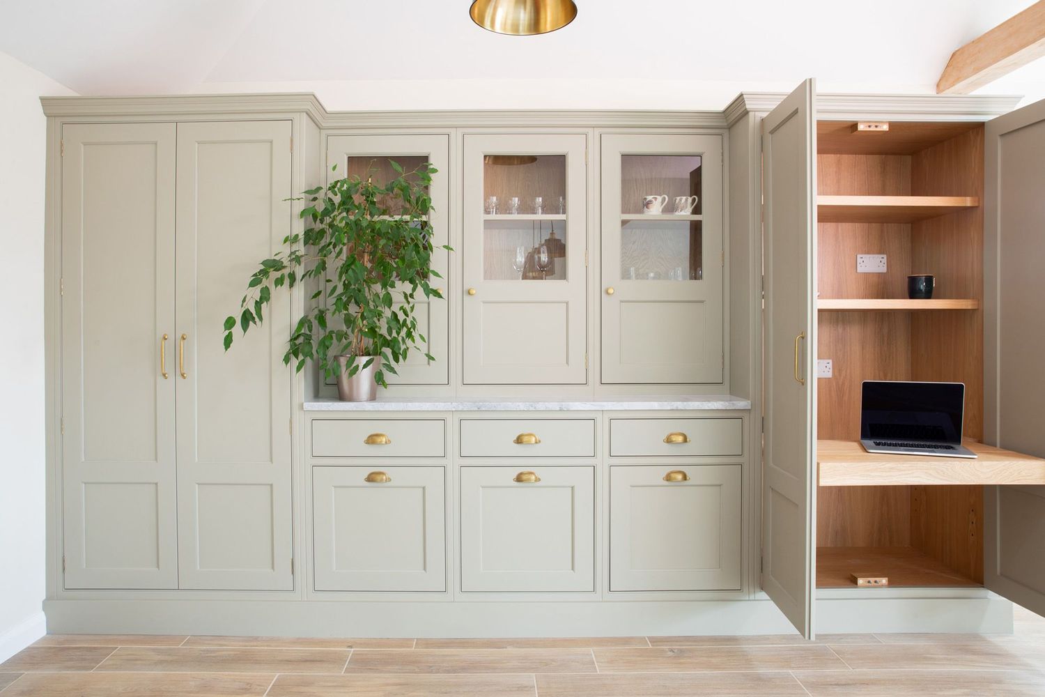 Light gray built-in cabinet with glass doors, drawers, and a houseplant adds storage to a modern home office space.