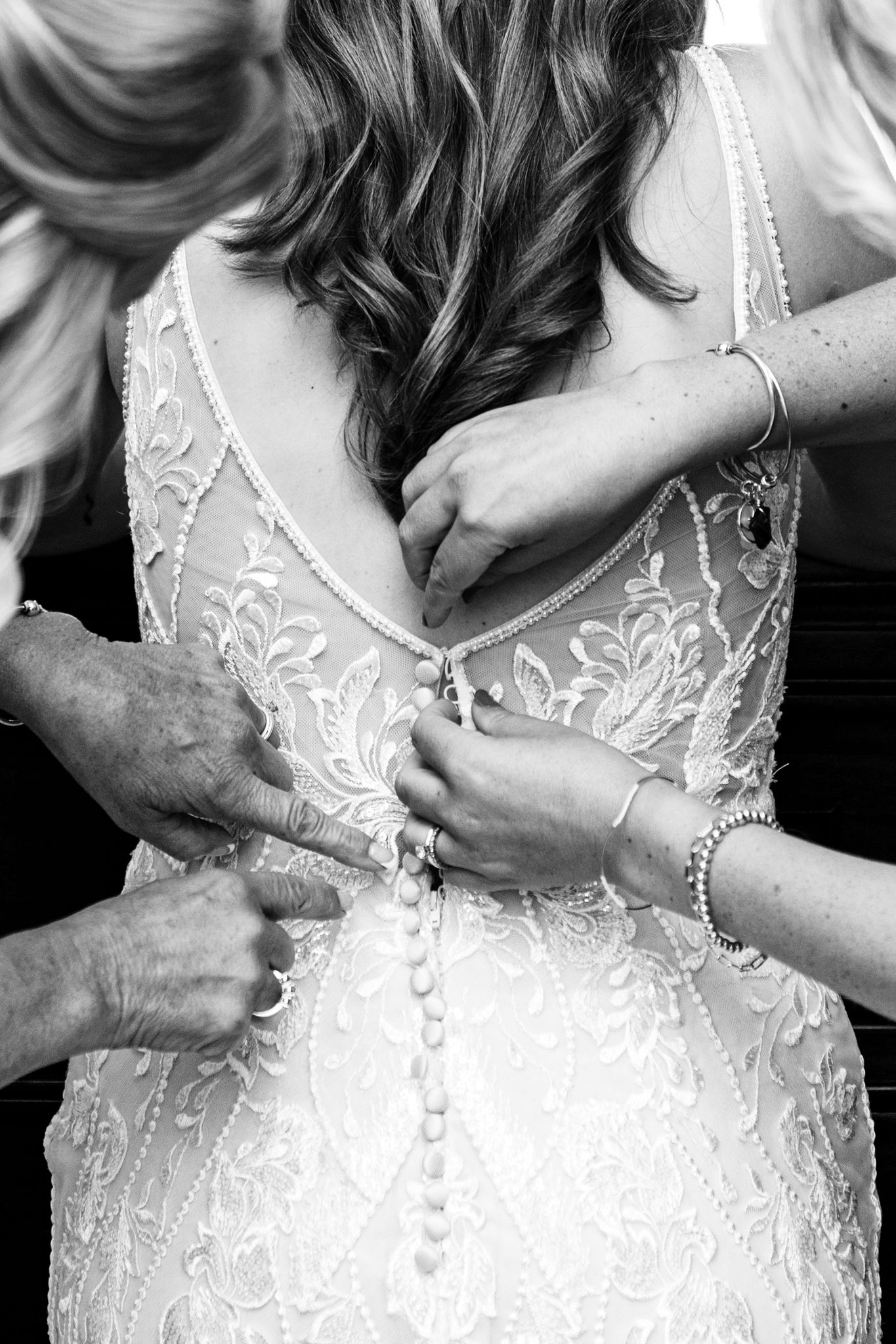 Black and white close-up of hands fastening buttons on a detailed lace wedding gown.