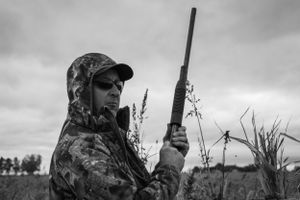Hunter in camouflage gear holding rifle in black and white photo.