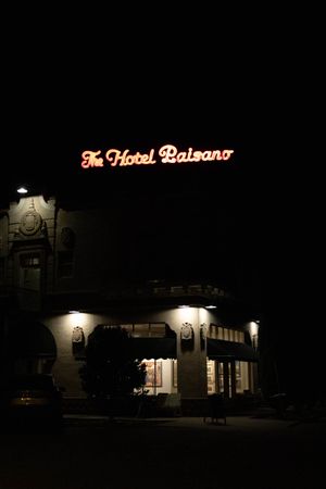 The Hotel Balzano illuminated sign glows against a dark night sky above a dimly lit Spanish-style building entrance.