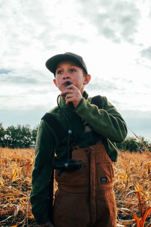 Youth in workwear and cap standing in golden cornfield.