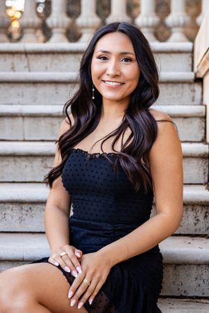 A portrait of someone in a black formal dress sitting on stone stairs.