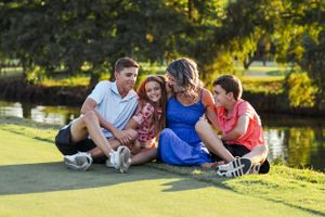 Family relaxing together on grass near pond during sunny afternoon.