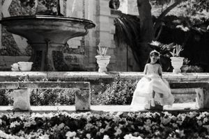 Garden setting with stone urns and colorful flower beds creates an elegant backdrop.