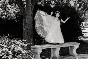 A couple in wedding attire poses for romantic photos under trees in a garden.