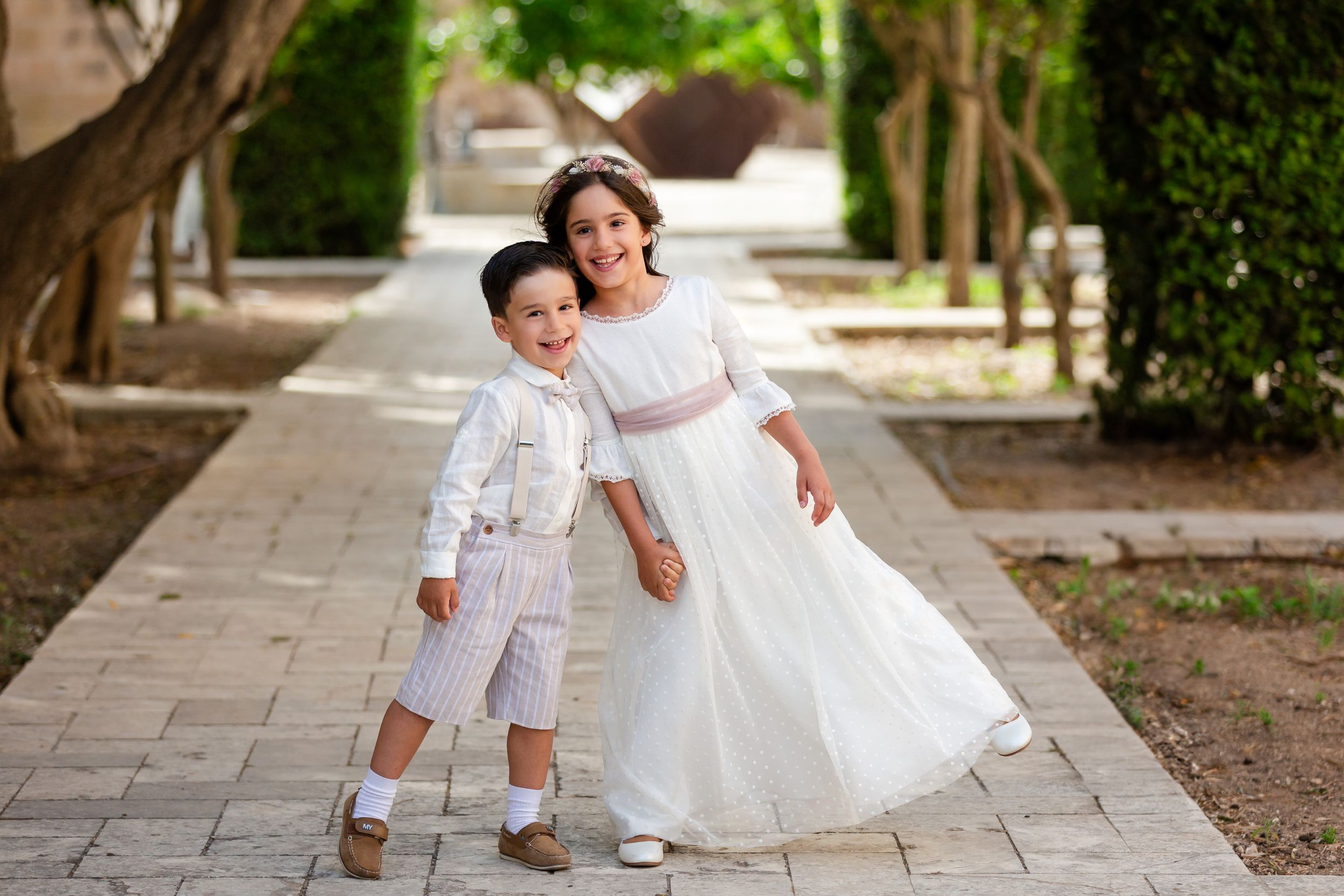 A white lace dress twirls gracefully on a stone pathway in a garden setting.