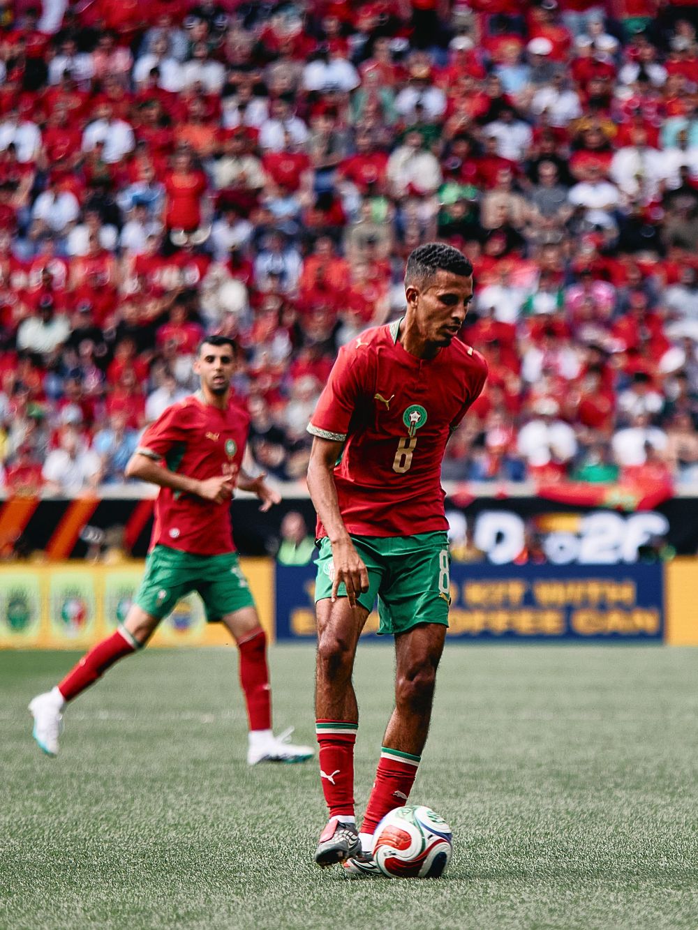 Morocco footballer wearing number 8 red jersey dribbles ball during international match with packed stadium crowd.