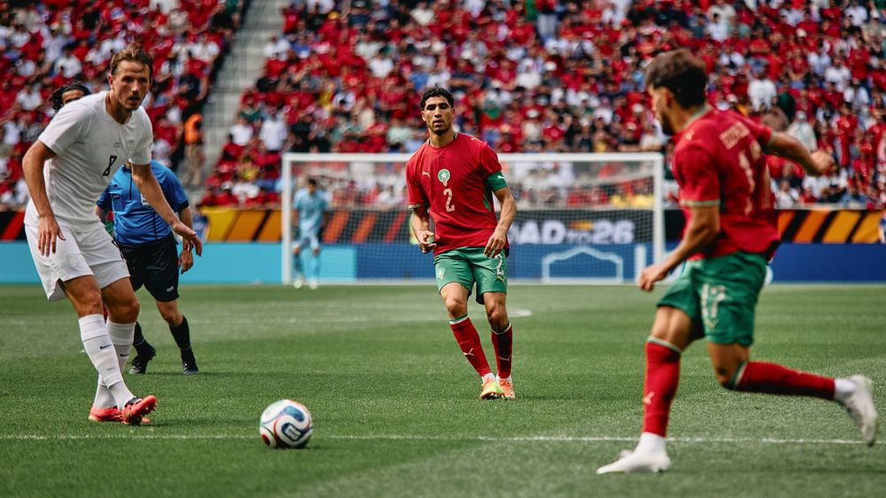 Portugal players in green and red kits compete against opponents in white during an international soccer match on a grass field.