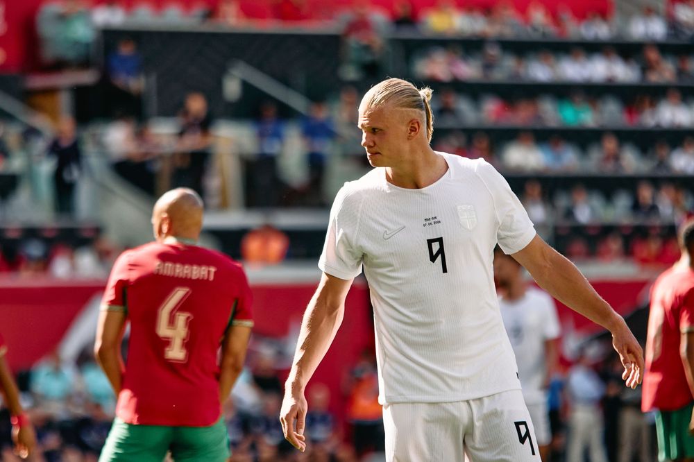 Soccer player wearing number 9 white jersey stands on field during match against team in red and green uniforms.