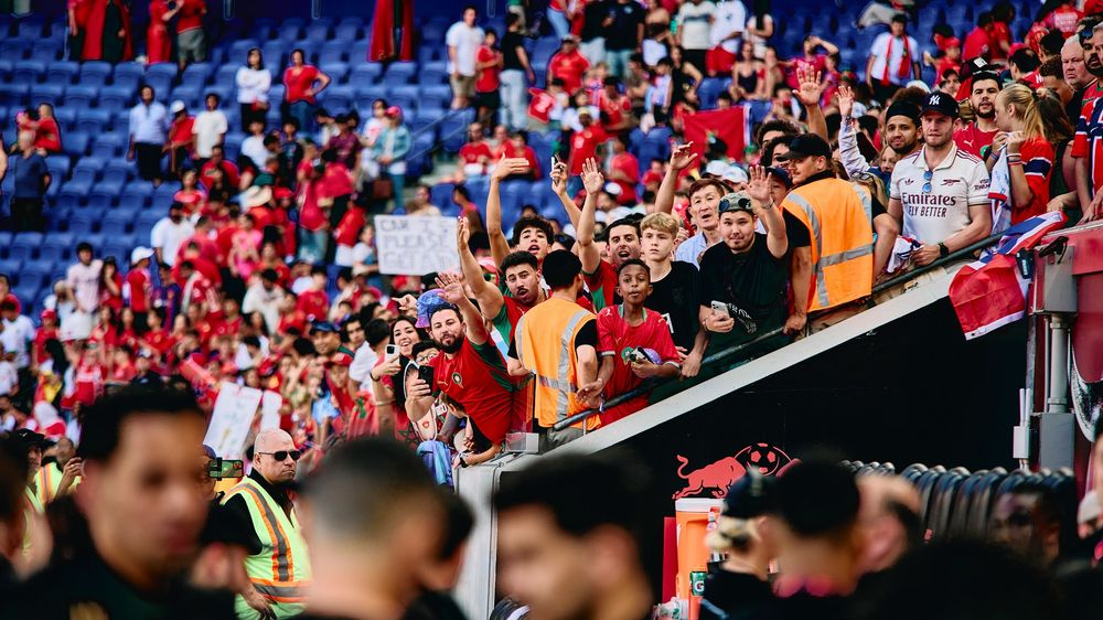 Crowd of fans in red and white jerseys cheering enthusiastically in a stadium during a soccer match.