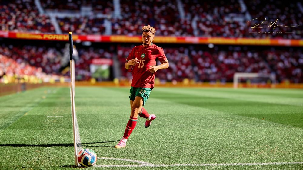 Portugal footballer in red kit dribbles near corner flag on green pitch during international match.