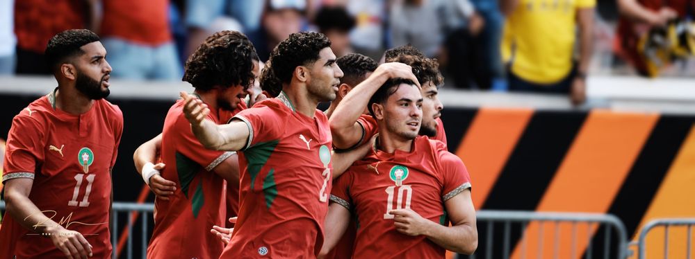 Morocco national football team players celebrating a goal together on the pitch during an international match.