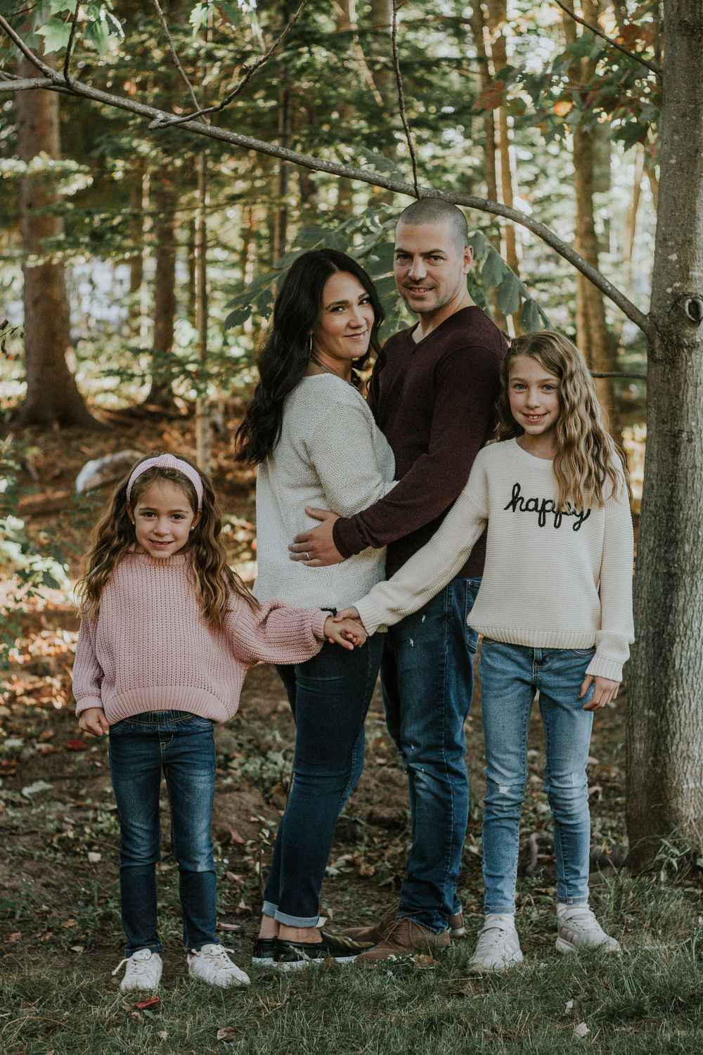 A family of four poses together in a forest during autumn, wearing cozy fall sweaters.
