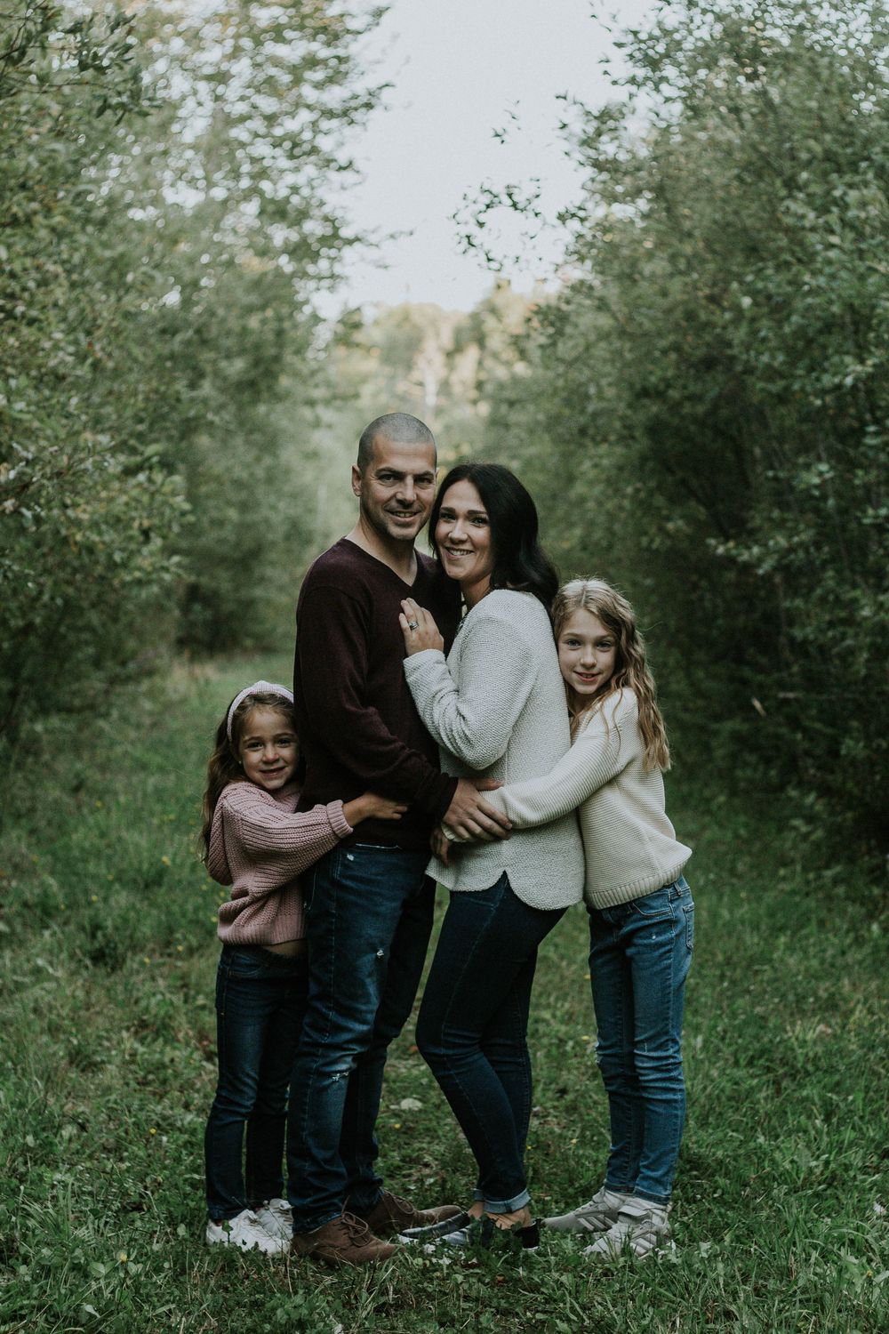 A loving family of four embraces in a lush green orchard pathway during fall season.