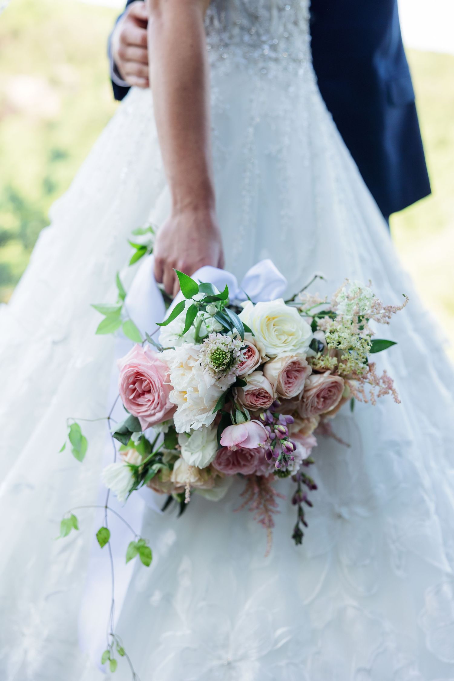 A white and pink bridal bouquet with roses and greenery against a wedding dress.