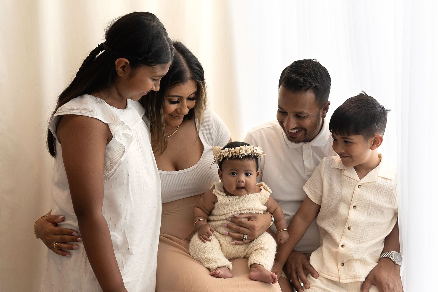 A beautiful family of five wearing white and cream colored outfits sits together and shares a tender moment.