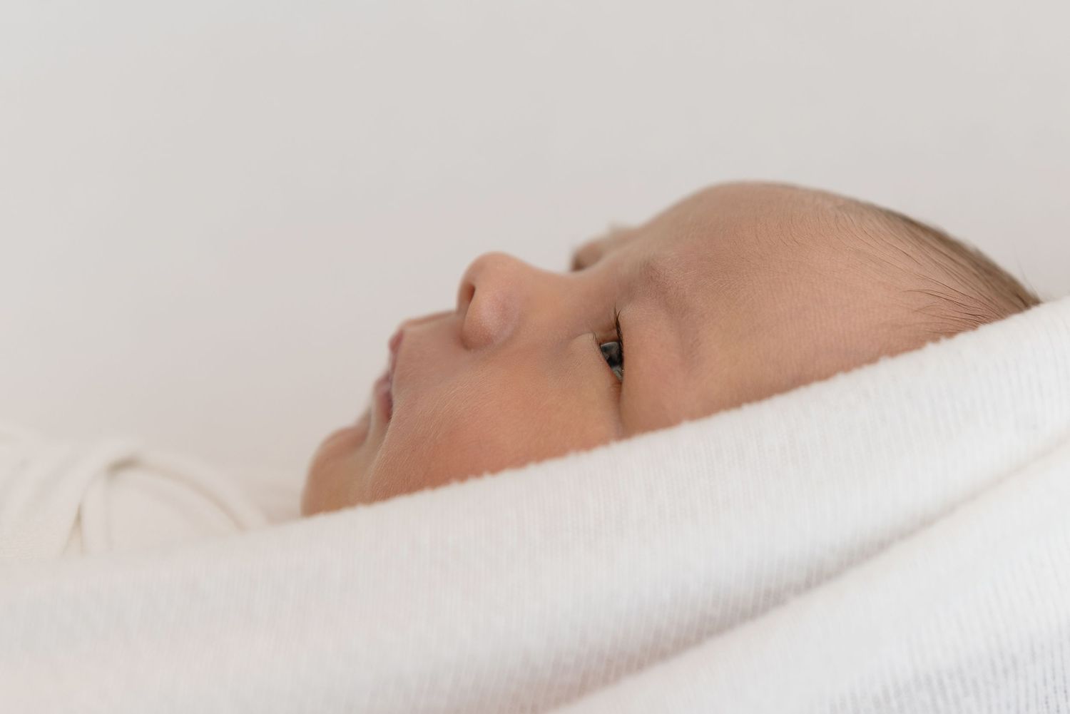 Close up view of baby wrapped in soft white blanket resting peacefully.