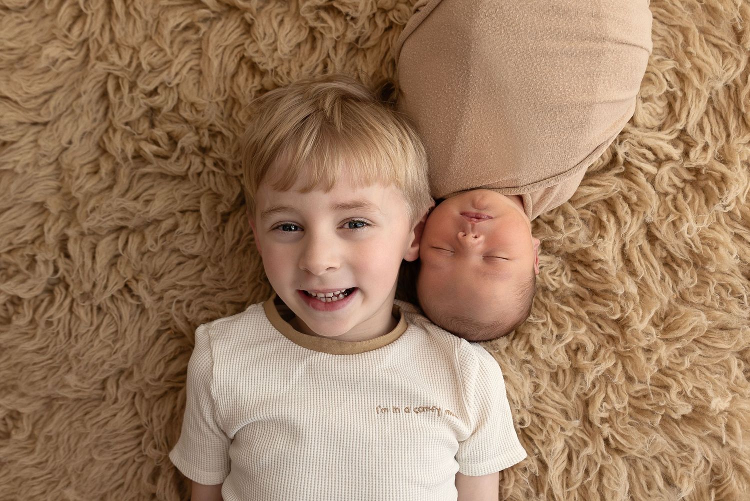 Siblings lying on cozy beige carpet sharing a joyful moment together.