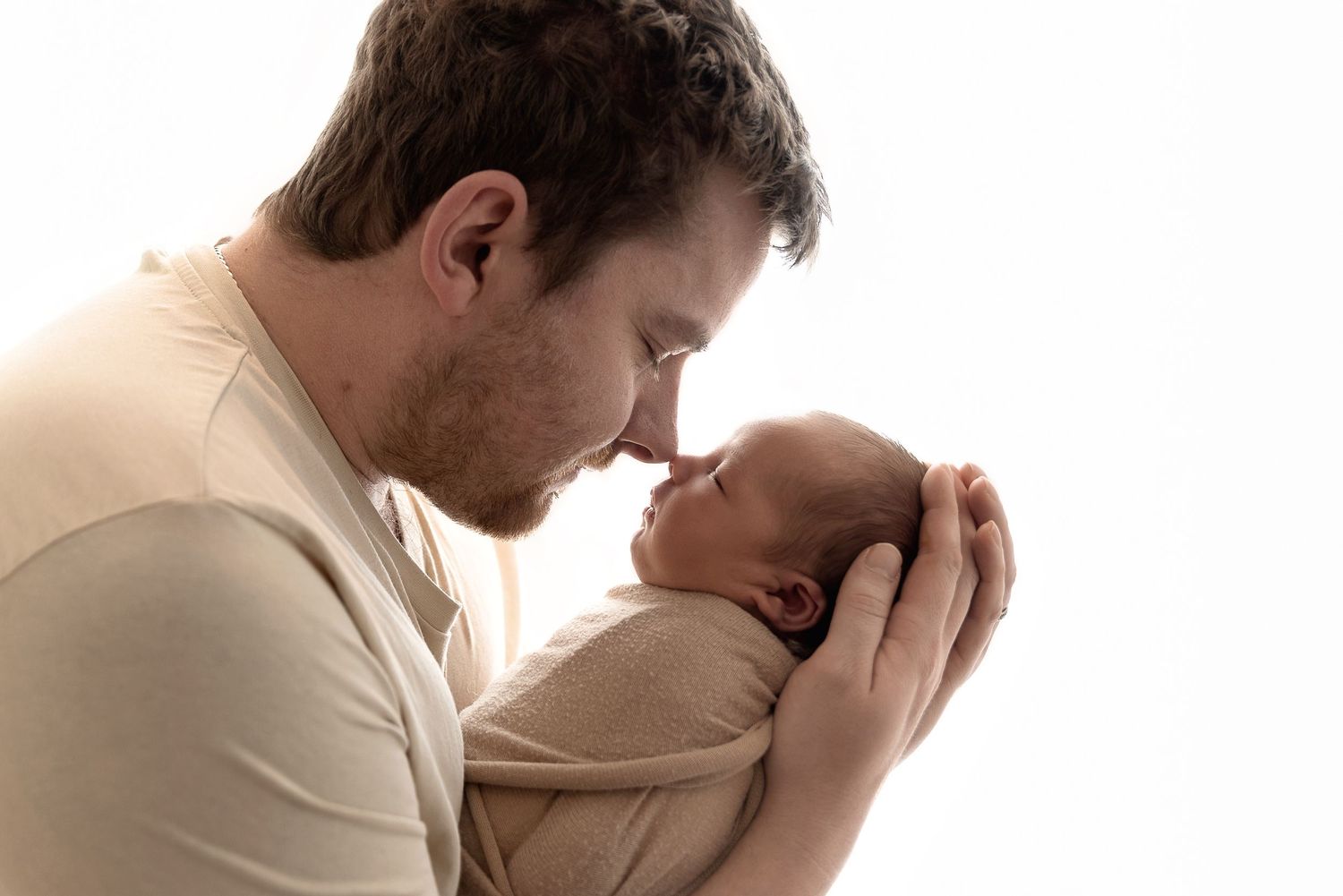 A tender moment between parent and newborn baby, with gentle cradling and a loving gaze against white background.