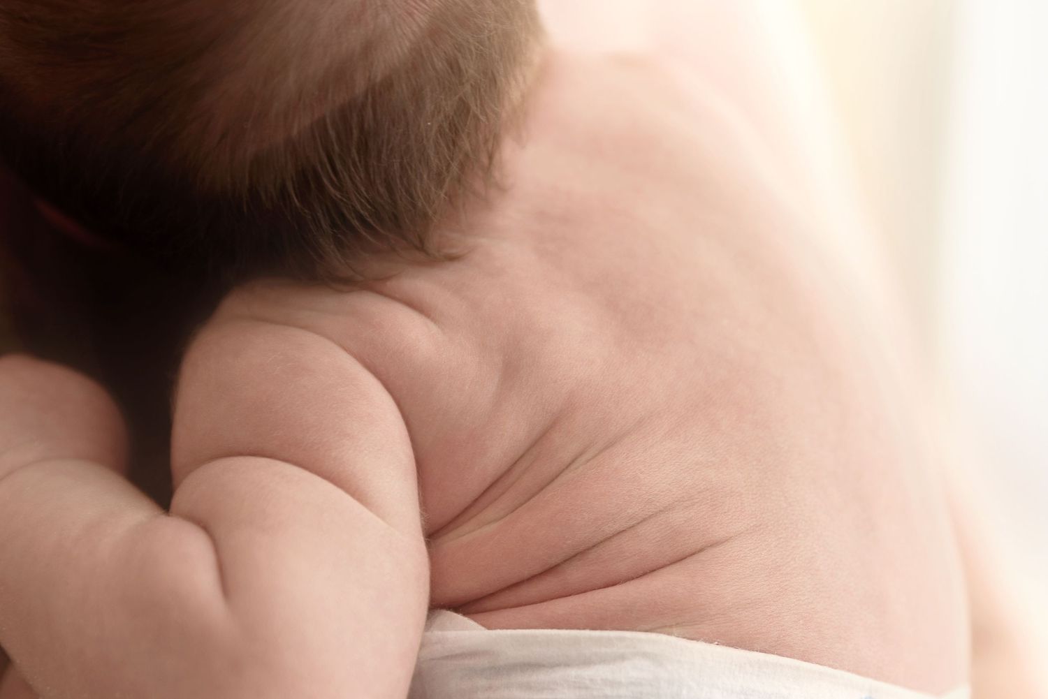 A tiny newborn baby's hand rests gently on top of a parent's larger palm in soft lighting.