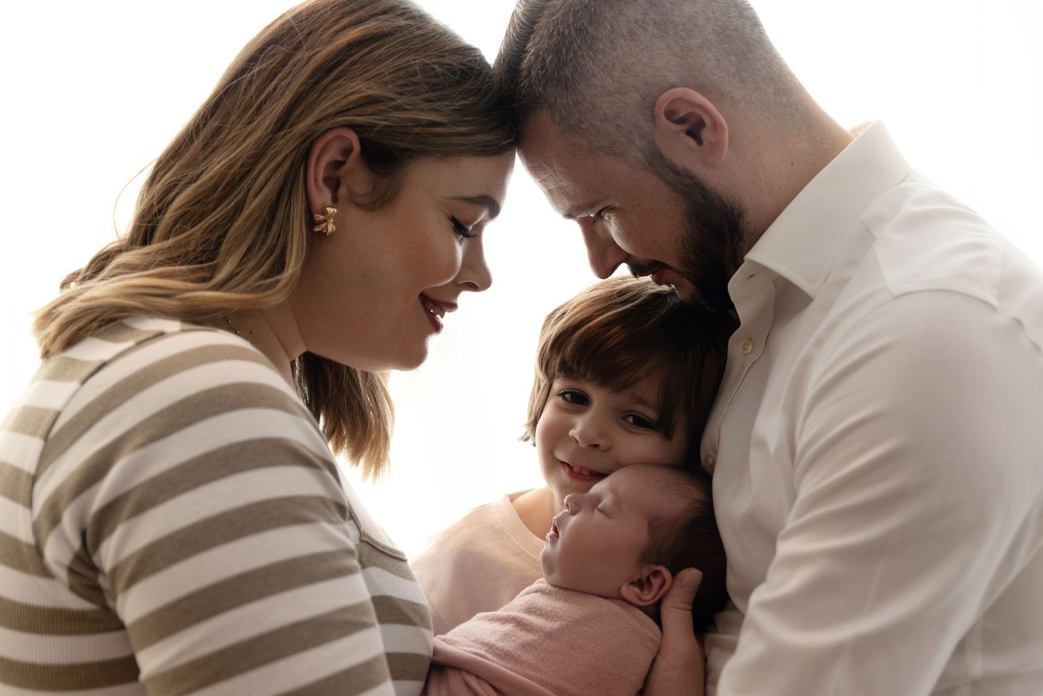 An intimate family portrait captures a tender moment as they embrace and lean in close together.