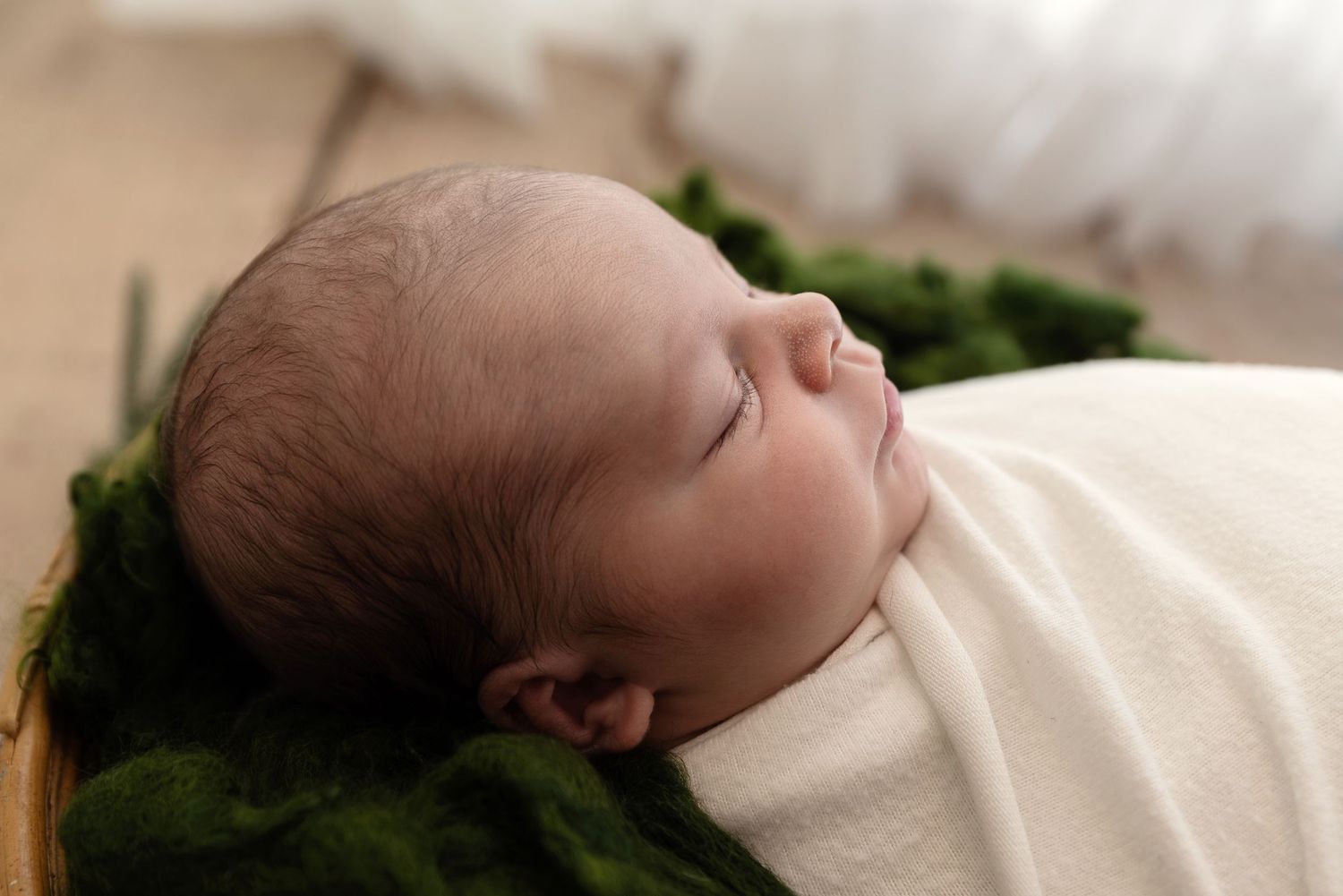 Sleeping baby rests peacefully on green moss-like textured blanket in soft lighting.