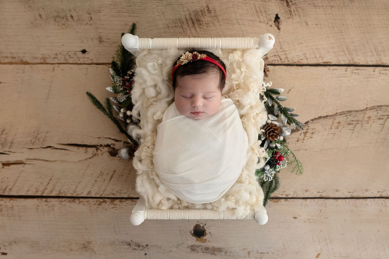Newborn swaddled in white fabric on cozy textured blanket with floral accents and wooden backdrop.