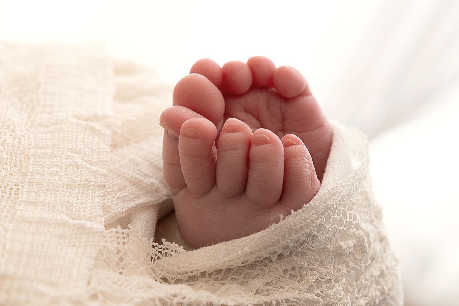 A tiny baby's hand grasps gently while resting on soft white fabric.