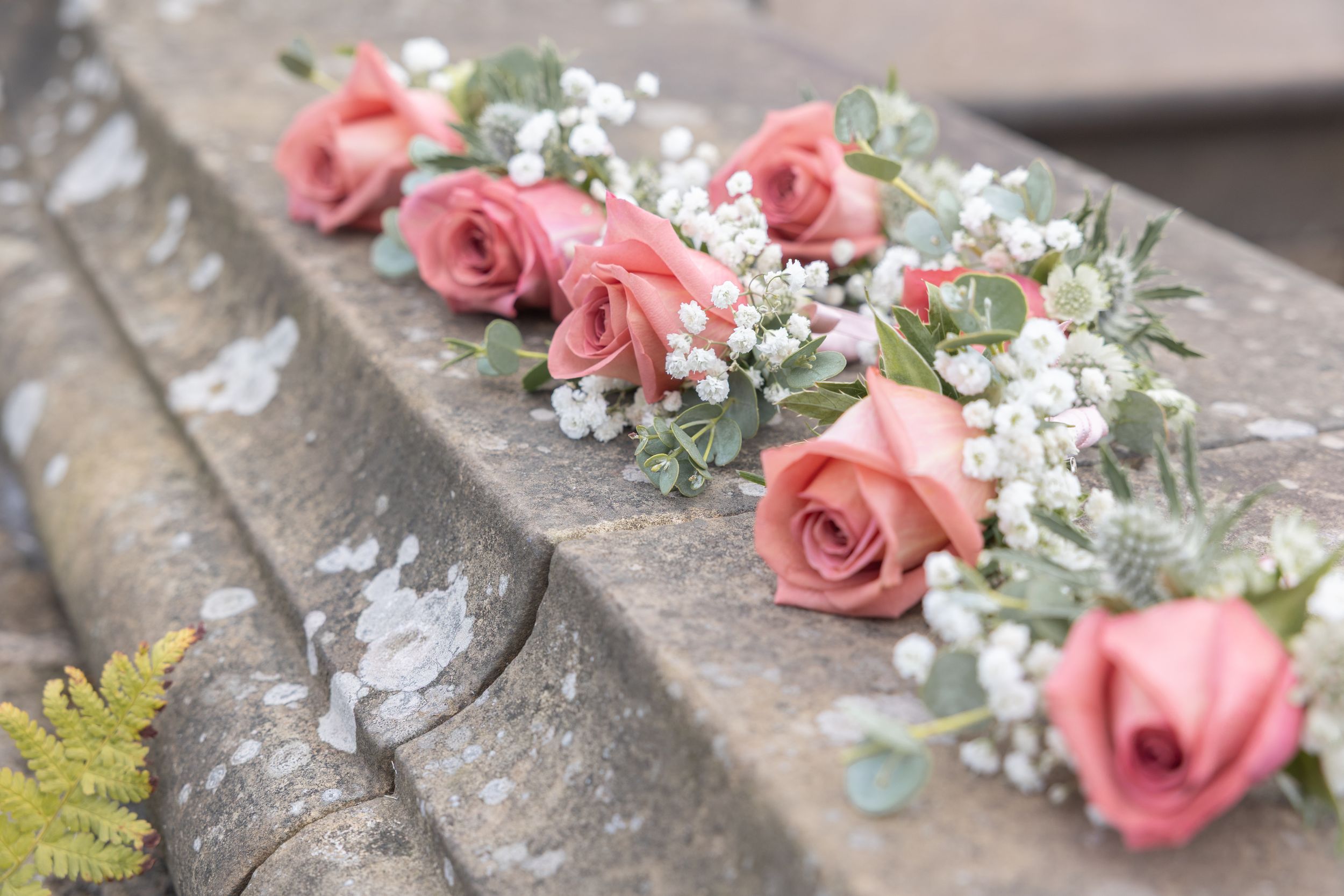 Pink roses and baby's breath flowers arranged in a line on weathered stone steps create a romantic wedding decoration.