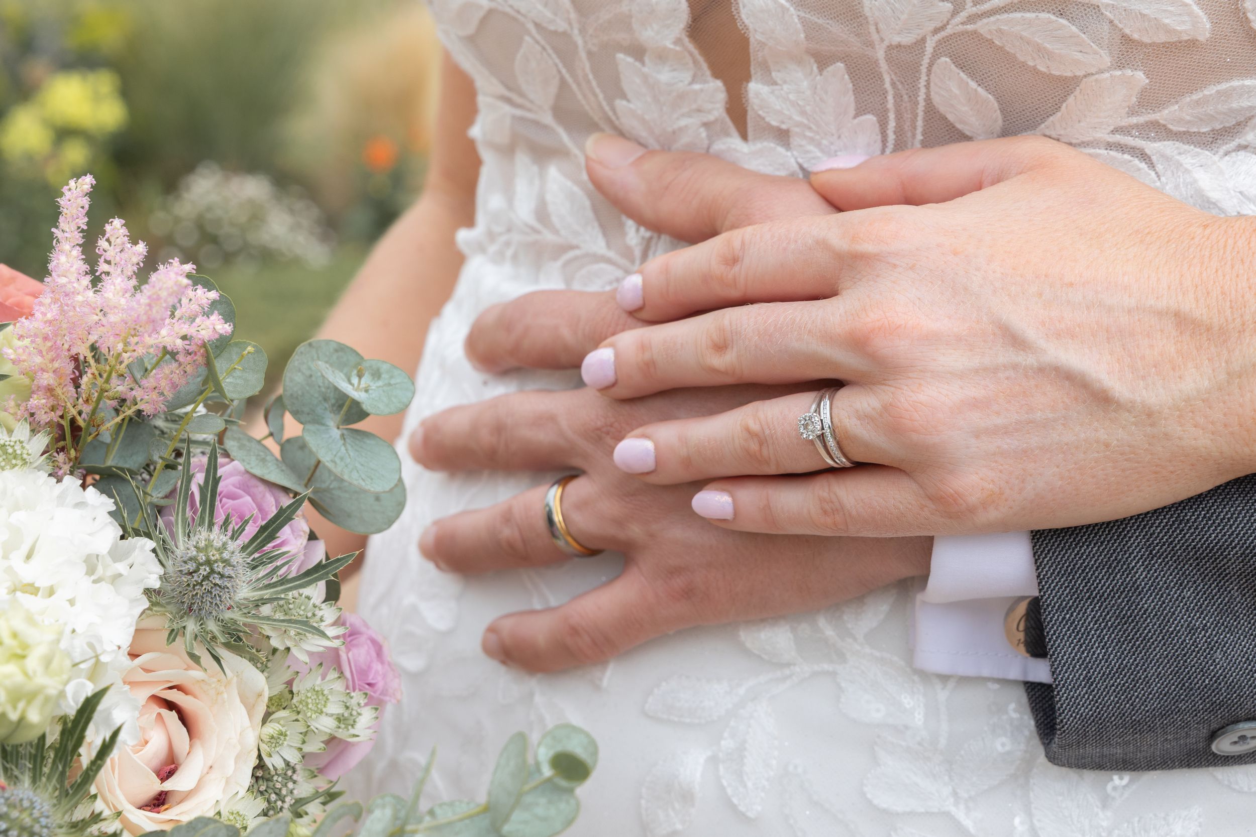 Close up detail shots of wedding rings and hands with pink and white floral accents in the background.