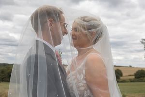 A romantic wedding moment captured with a flowing veil against a cloudy rural backdrop.