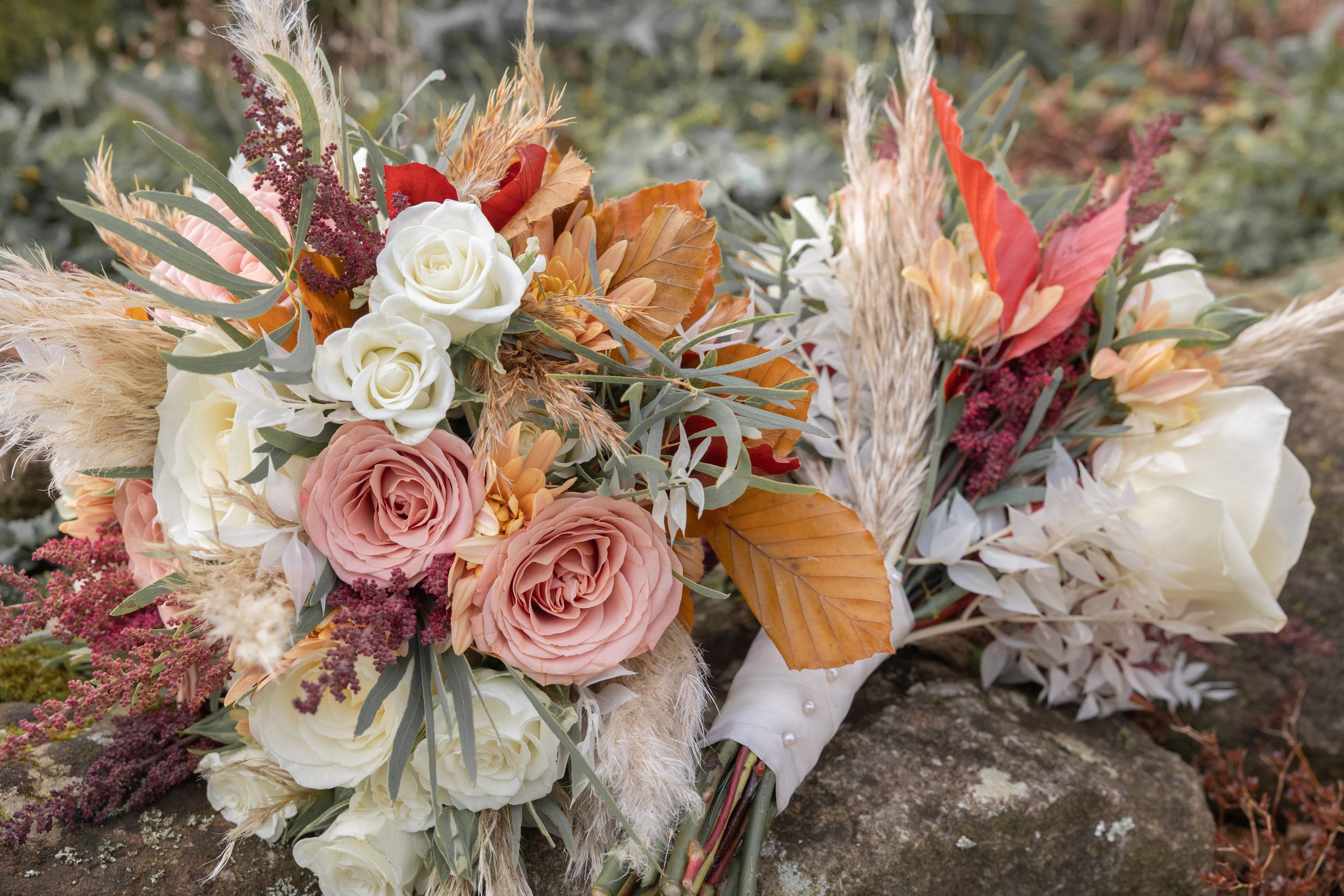 Beautiful boho wedding bouquet with blush pink roses, white flowers, dried pampas grass and autumn foliage on stone surface.