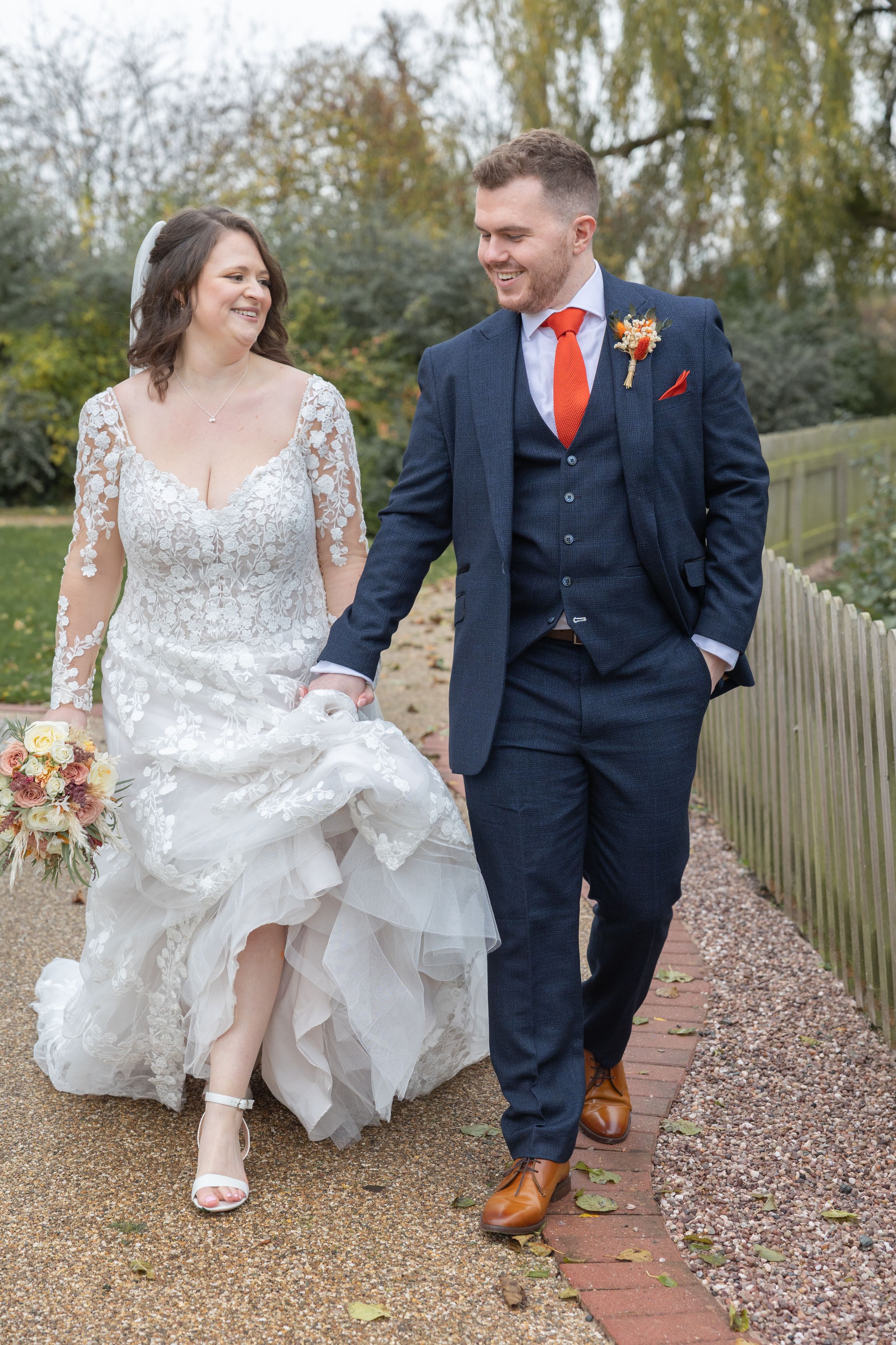 Wedding couple shows off their footwear while sitting on outdoor brick steps surrounded by autumn leaves.