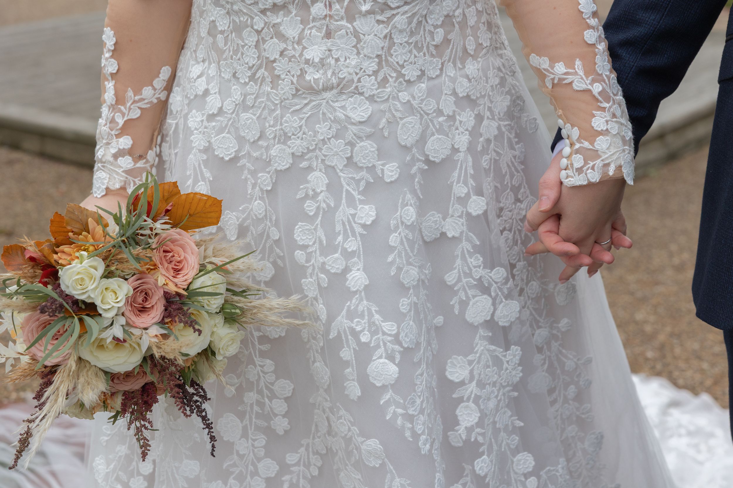 Close-up details of a bride's lace wedding dress, holding hands with groom and floral bouquet with peach and blush blooms.