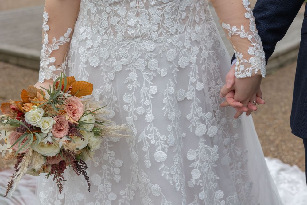 Close-up details of a bride's lace wedding dress, holding hands with groom and floral bouquet with peach and blush blooms.