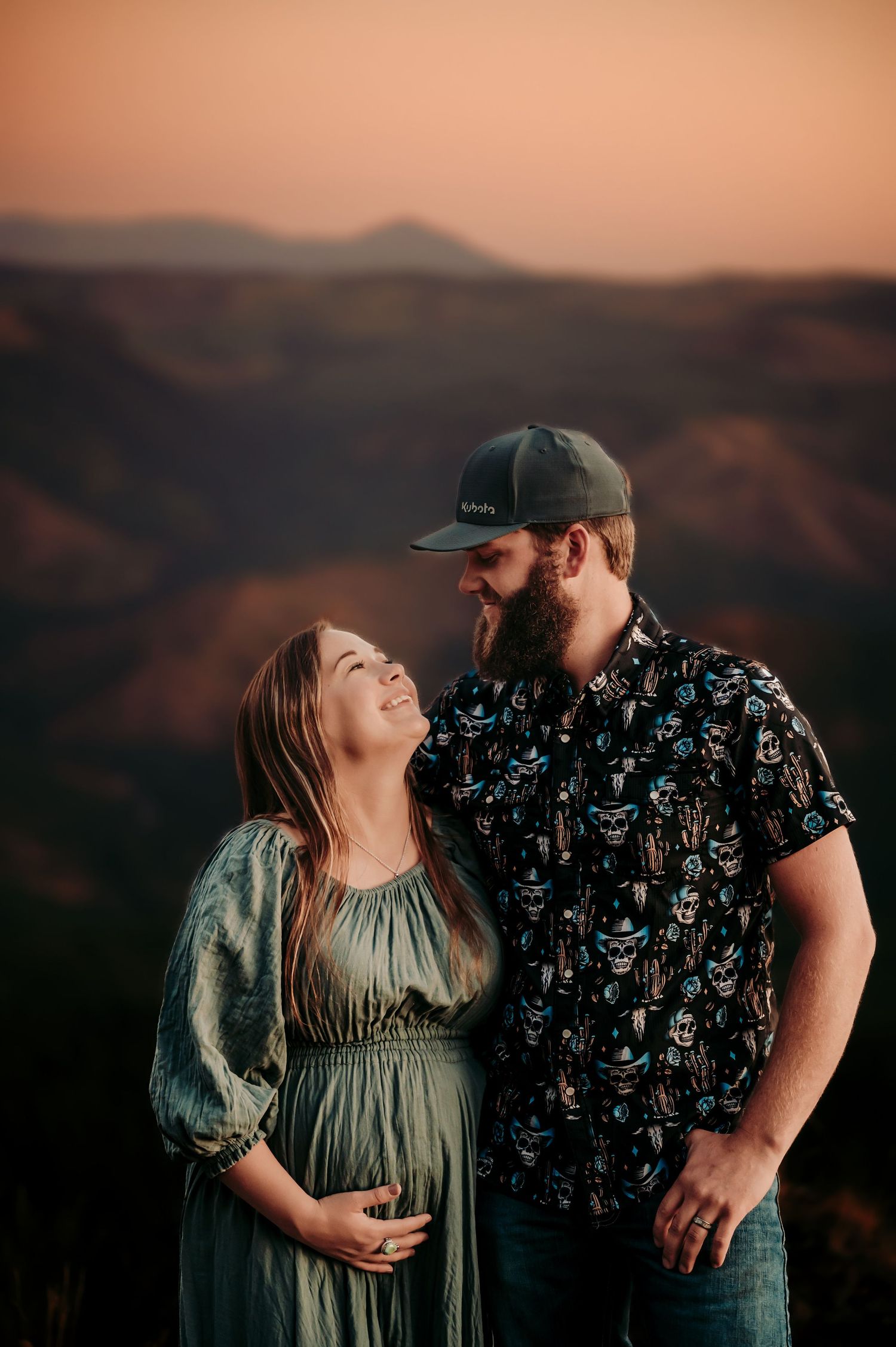 Couple shares intimate moment during mountain sunset maternity photoshoot.