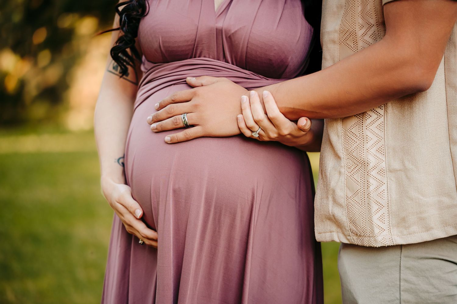 Tender maternity moment captured in soft natural lighting with mauve dress details.