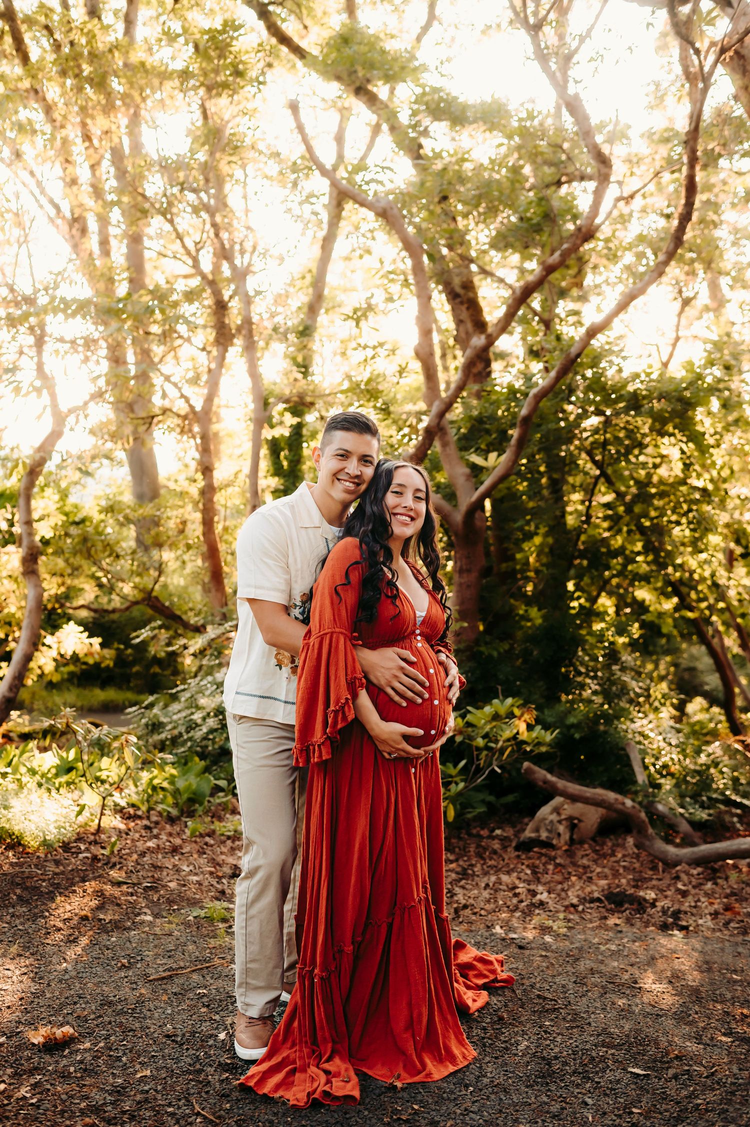 Couple embracing in a wooded setting wearing red velvet and white clothing at sunset.