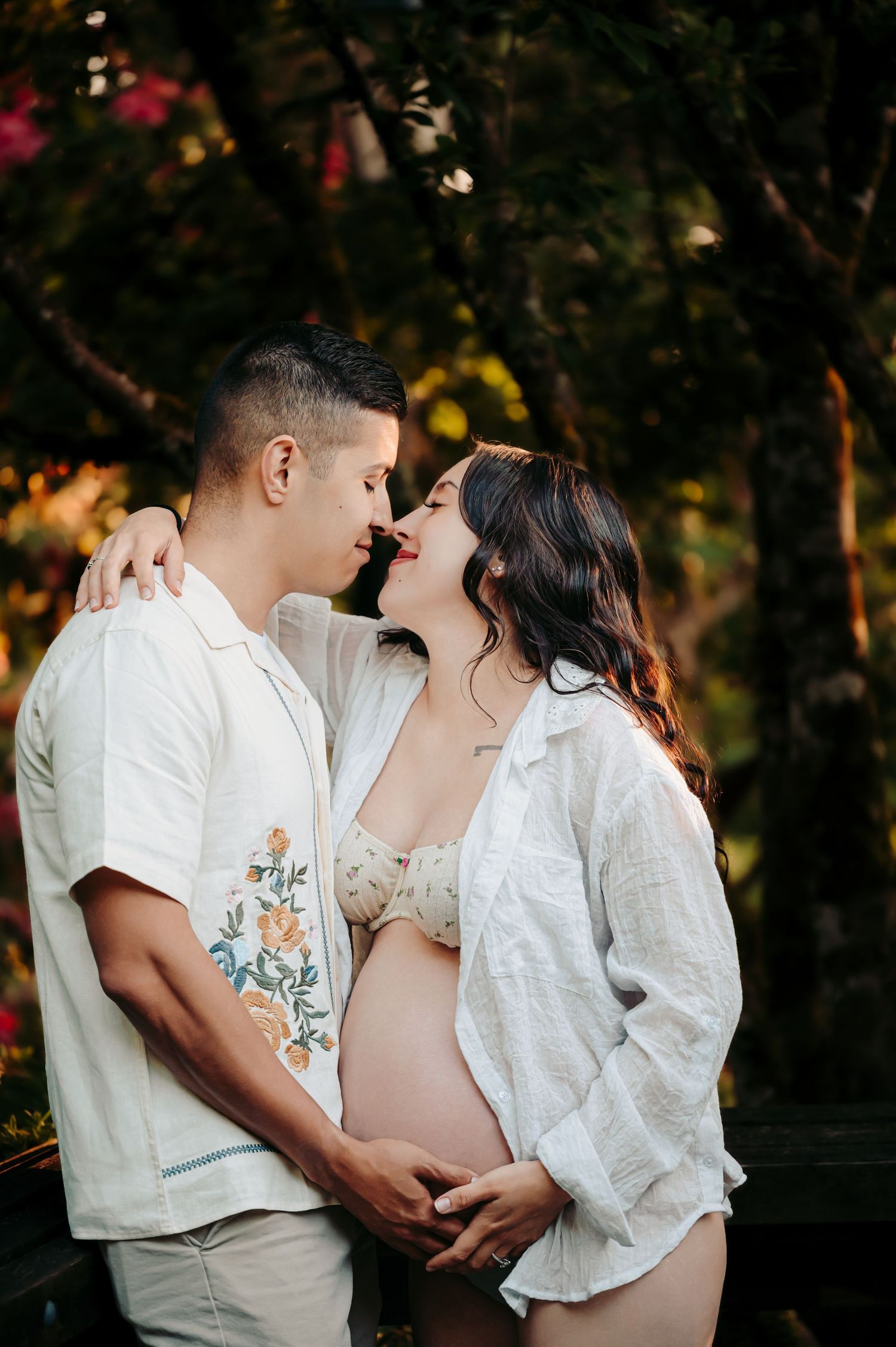 Intimate maternity portrait session with couple in white clothing against forest backdrop.