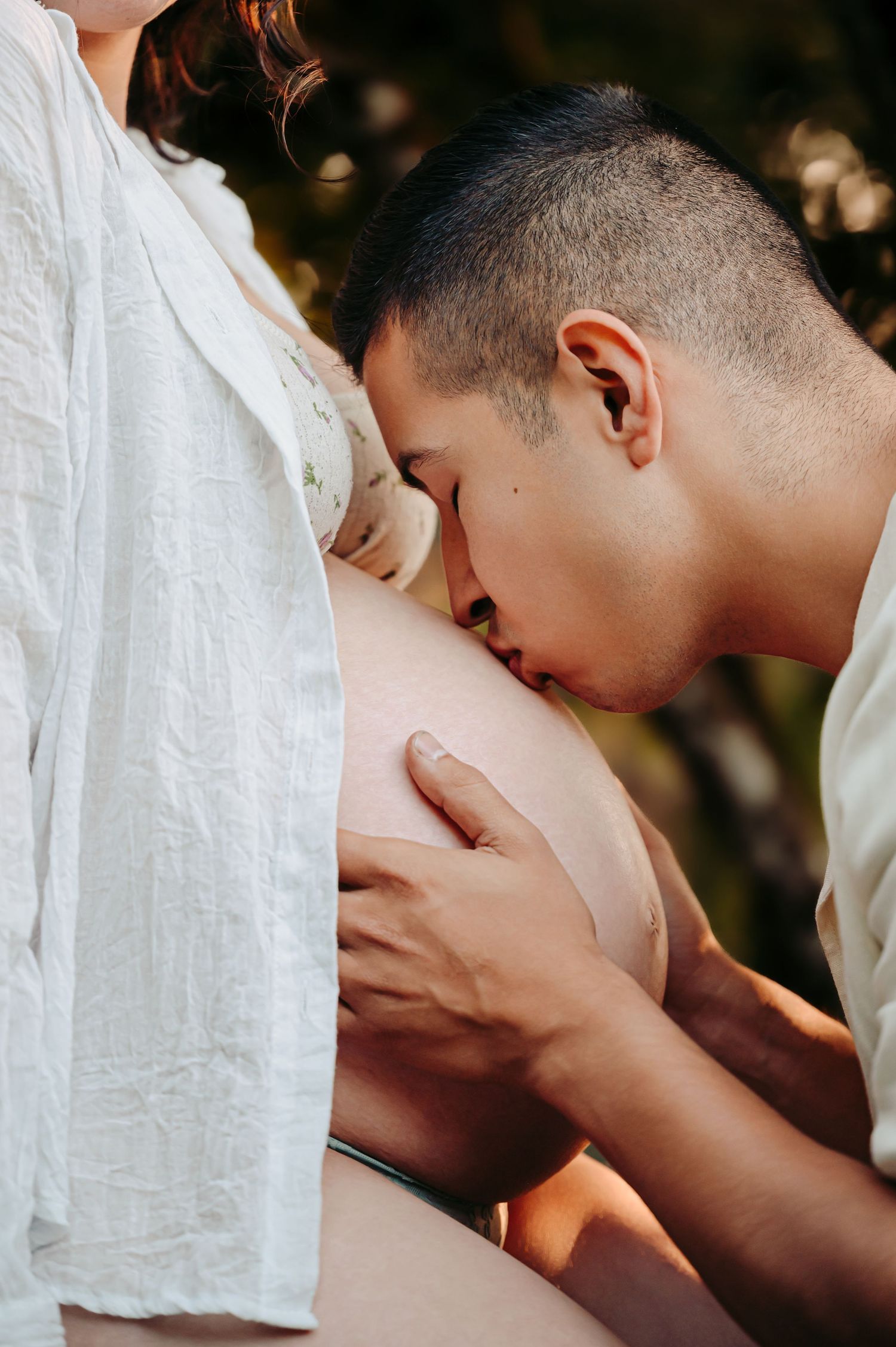 Tender maternity moment captured in natural lighting with soft white clothing.