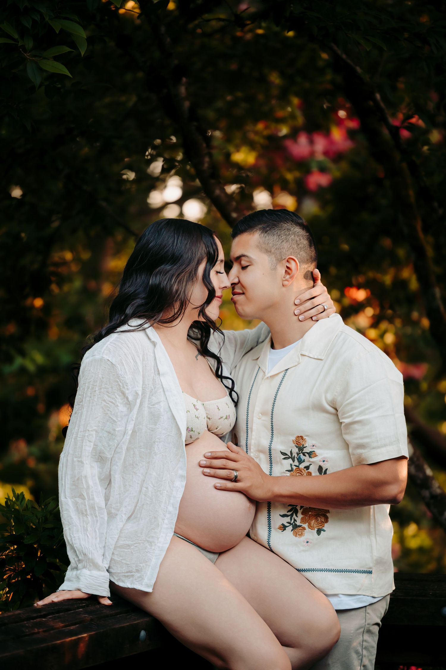 Romantic outdoor maternity photos with couple in white attire during golden hour.