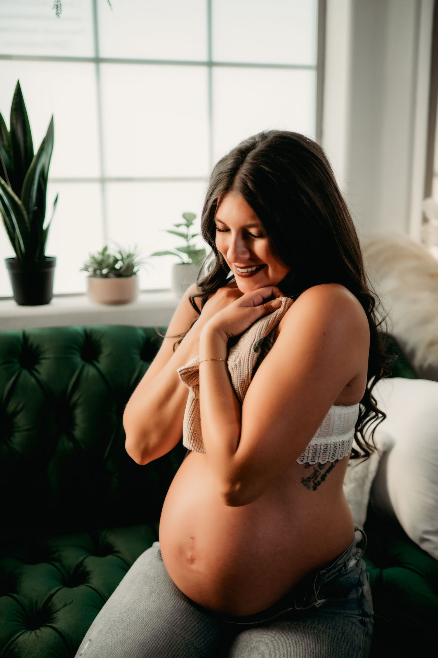 Intimate maternity photography session with soft window light and indoor plants.
