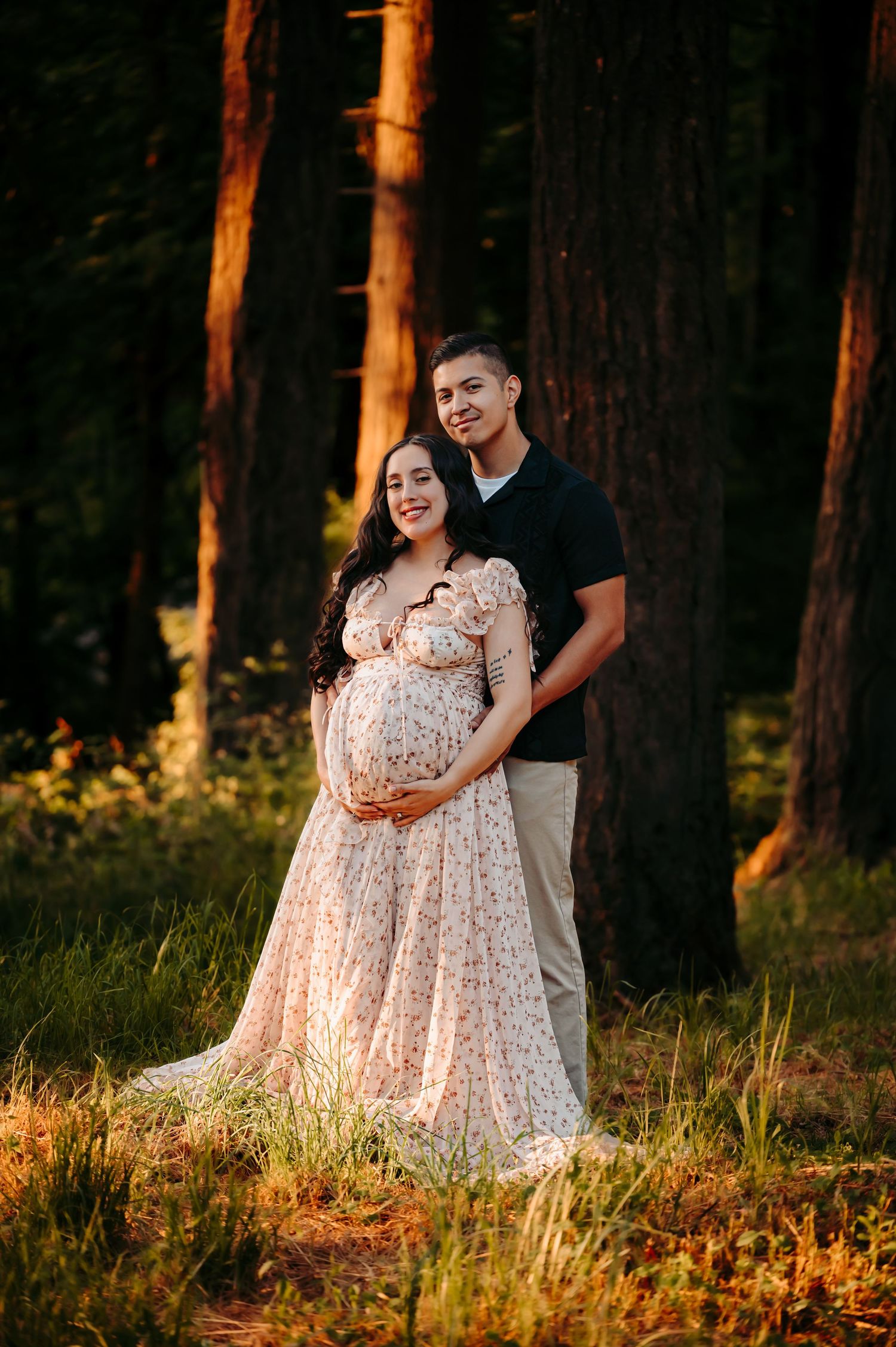 Couple sharing intimate moment in forest setting with flowing floral dress.