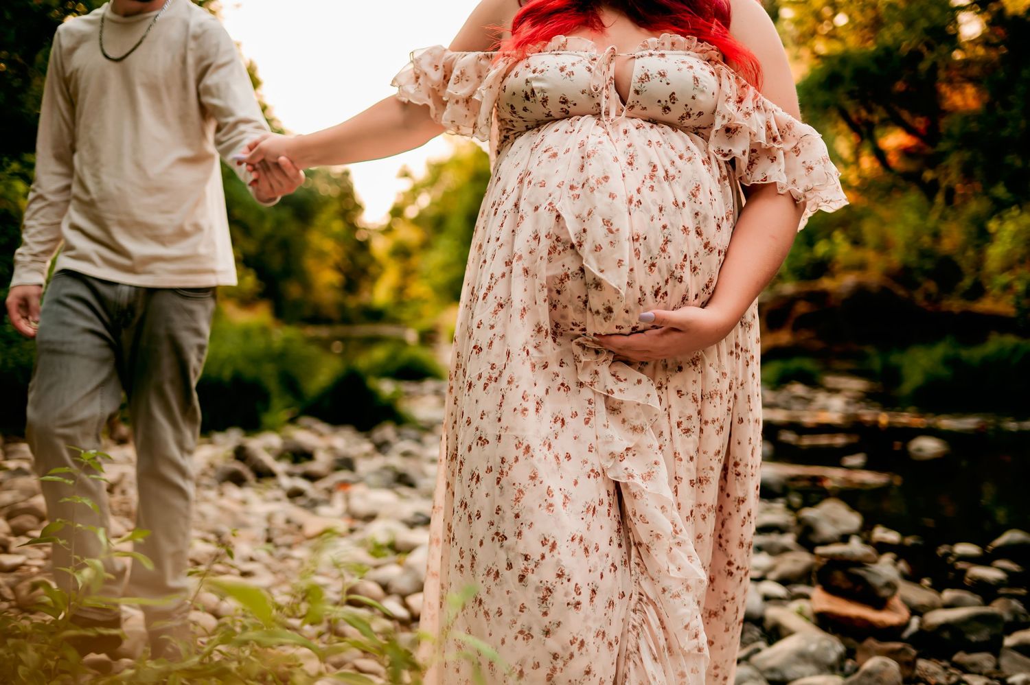 Maternity photos captured on rocky riverbed with flowing dress and natural lighting.
