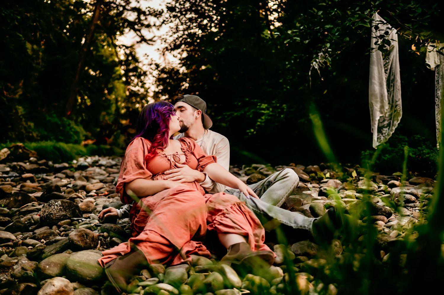 Intimate maternity session among rocks and trees with warm sunset lighting.