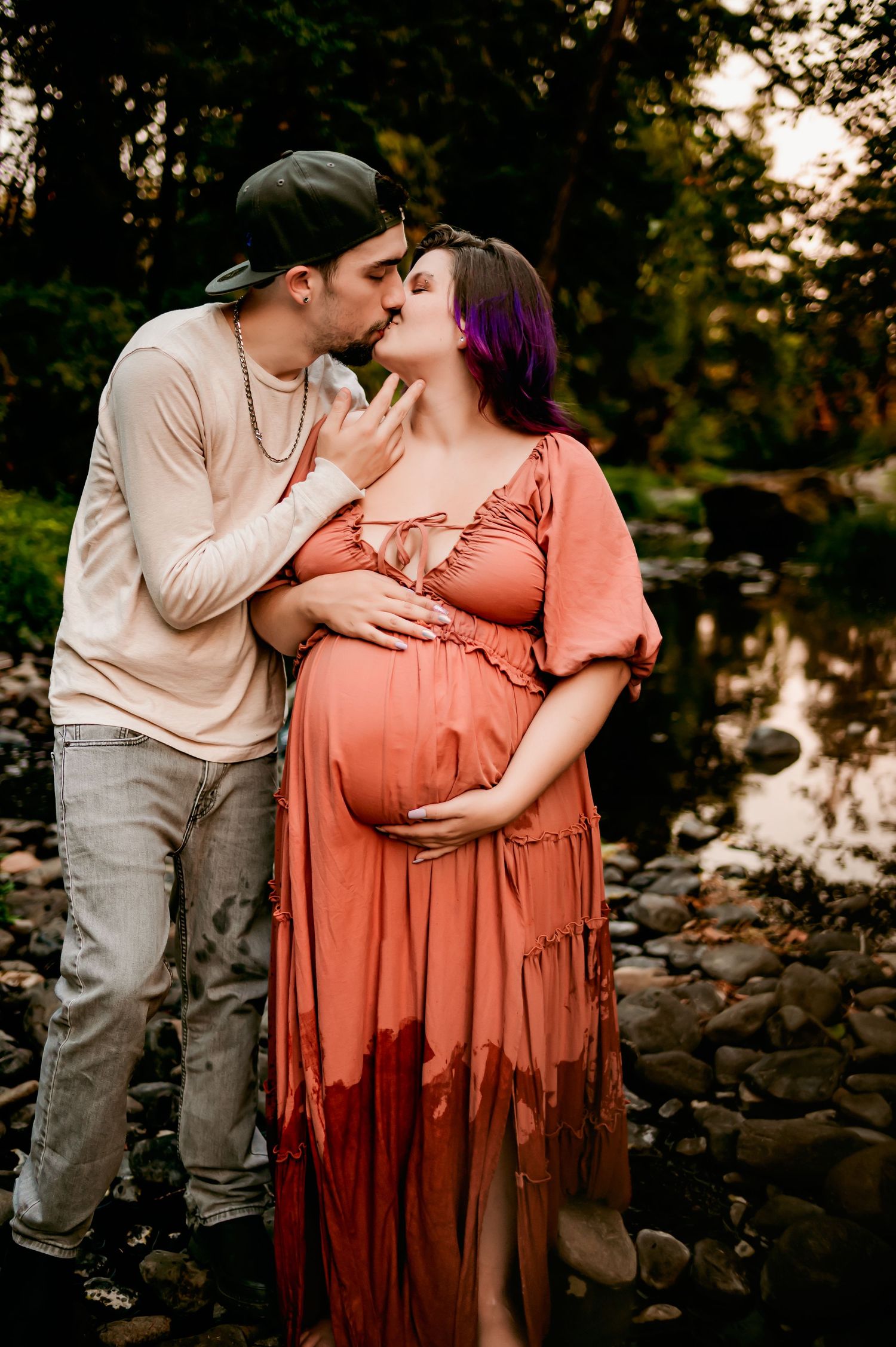 Tender moment between couple during riverside maternity photoshoot at golden hour.