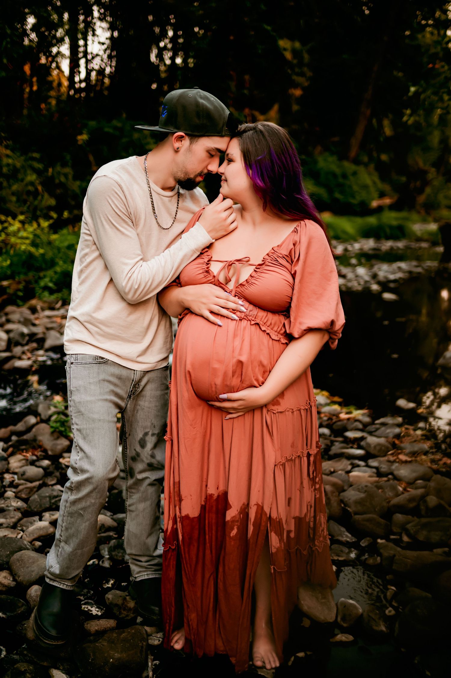 Intimate maternity portraits by stream with couple in casual attire during sunset.