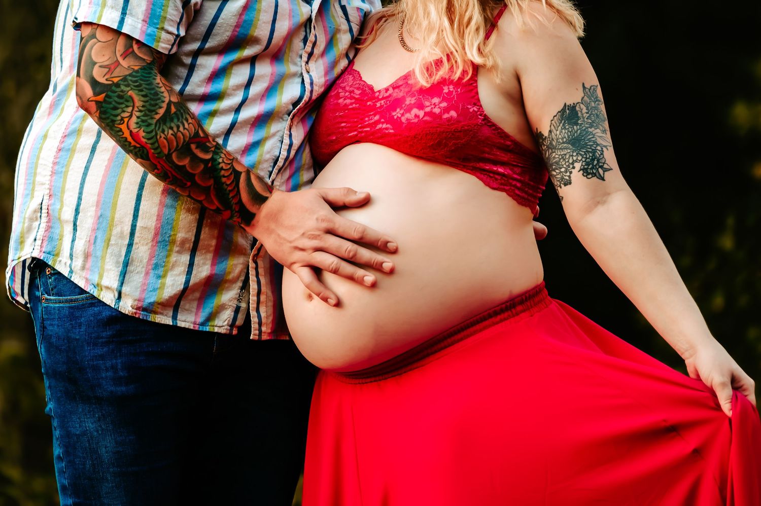 Close-up maternity photo showing hands cradling pregnant belly in red dress.